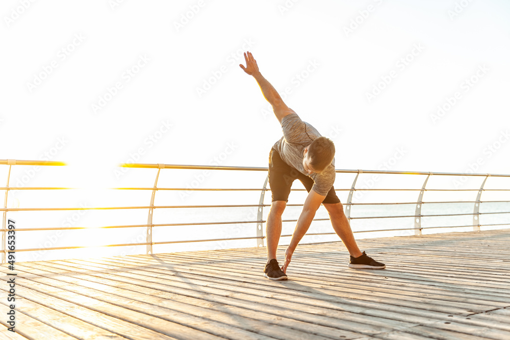 Young athletic man practicing warm-up before exercising on beach in the early morning. Healthy lifestyle