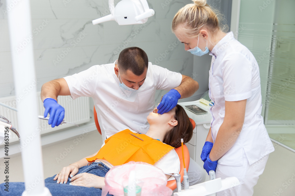 Obraz premium Dentist with assistant examines the oral cavity of female patient in dental clinic. Visit to the dentist. Dental treatment