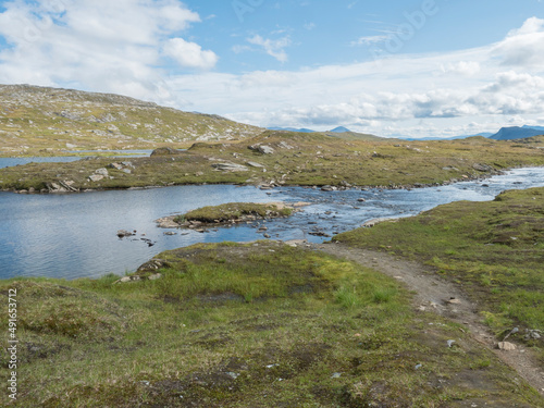 Beatiful northern landscape, tundra in Swedish Lapland with blue artic lake, green hills and mountains at Padjelantaleden hiking trail. Summer day, blue sky, white clouds