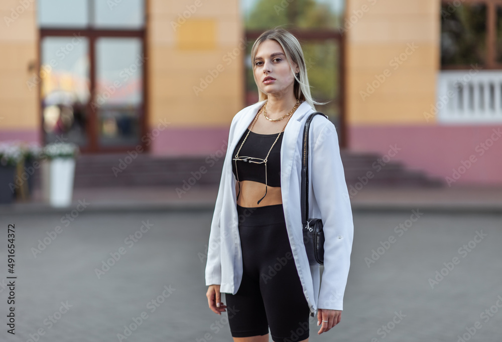 Young fashion woman in a white trendy jacket, leather bag in the city. Street fashion