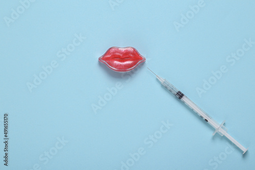 Lips and injection syringe with hyaluronic acid on a blue background. Lip augmentation concept. Minimalistic beauty still life photo