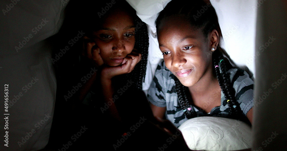 Two black teenagers girls using smartphone device at night under blanket