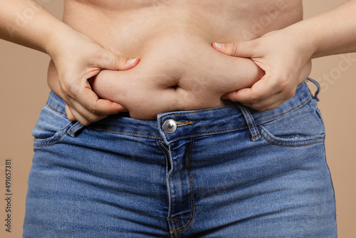 Foto Caucasian fat woman touching overweighted belly with hands wearing blue jeans