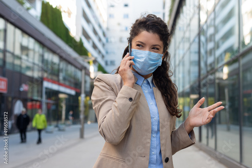 Business woman wearing face mask and talking with somebody on her mobile phone while walking © Dexon Dee