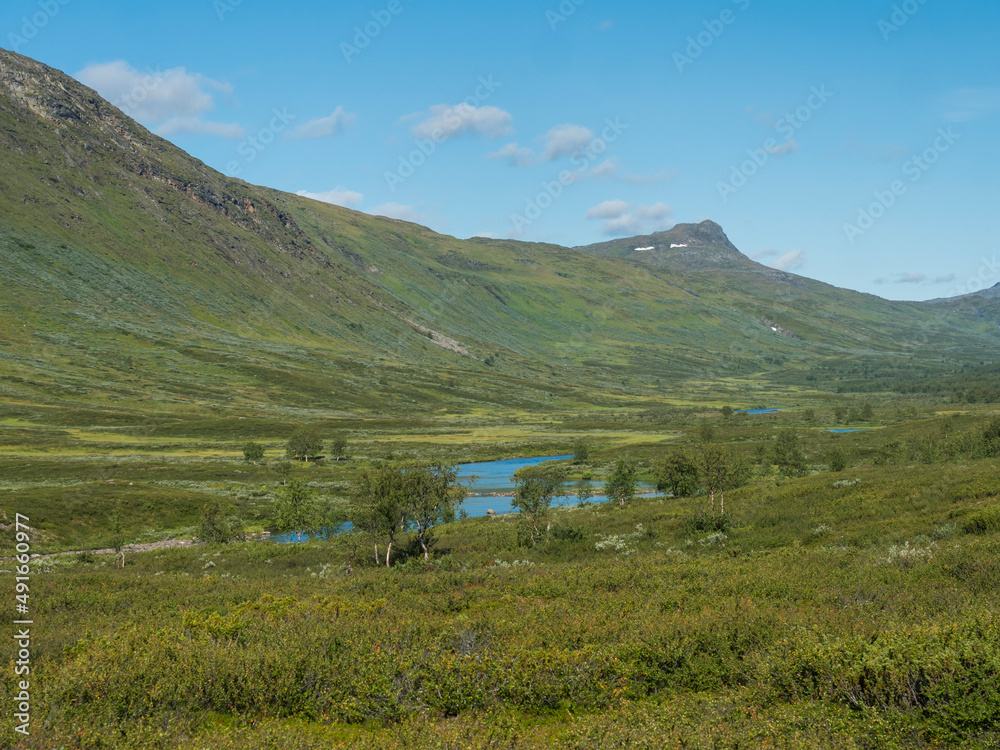 Beatiful northern landscape, tundra in Swedish Lapland with blue artic river and lake, green hills and mountains at Padjelantaleden hiking trail. Summer day, blue sky, white clouds Beatiful northern landscape, tundra in Swedish Lapland with blue artic river and lake, green hills and mountains at Padjelantaleden hiking trail. Summer day, blue sky, white clouds