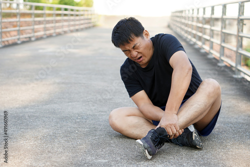 Asian Man runner gets hurt on his painful ankle after running , jogging, exercise. Concept : injury ankle twist sprain accident in workout or sport. 