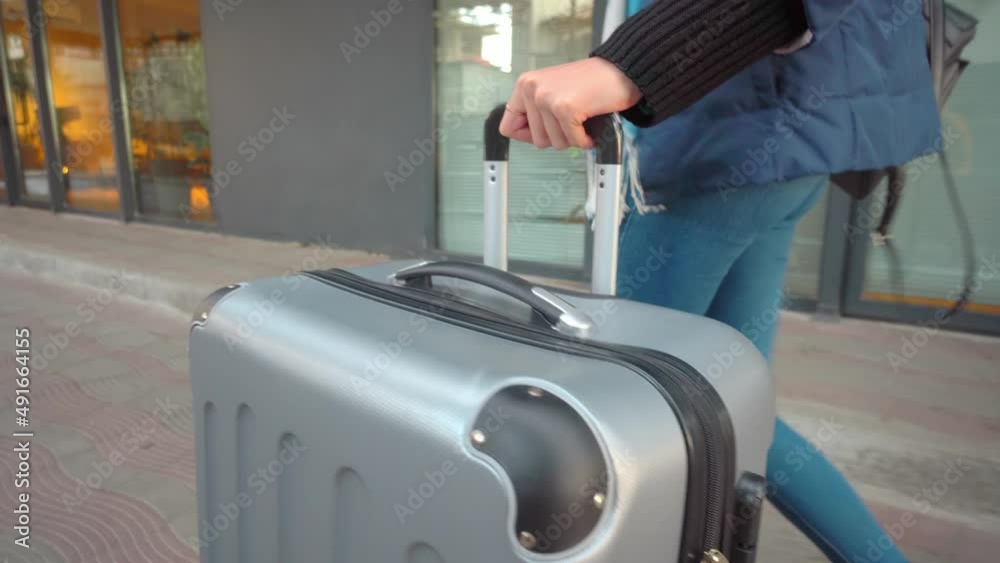 Close-up of a woman leaving the hotel with luggage. She rolls the suitcase down the street along the railing and the lobby. Suitcase close-up wide angle. A trip or a trip. Business trip. Close-up of a woman leaving the hotel with luggage. She rolls the suitcase down the street along the railing and the lobby. Suitcase close-up wide angle. A trip or a trip. Business trip.