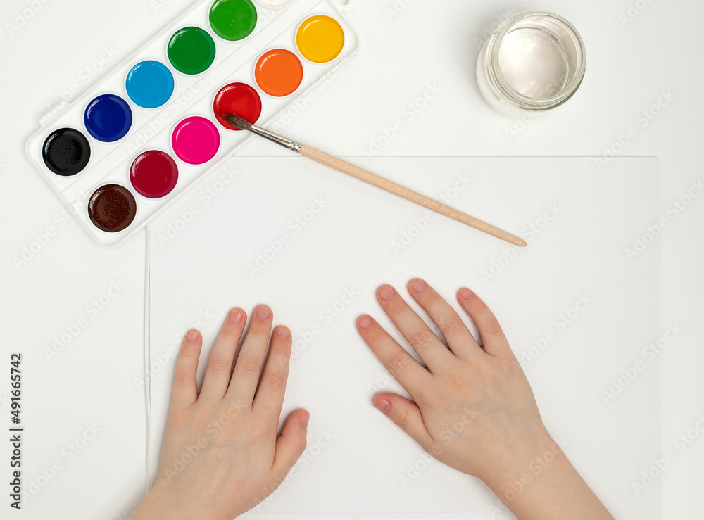 Children's hands begin to draw at a table with art supplies, top view Children's hands begin to draw at a table with art supplies, top view