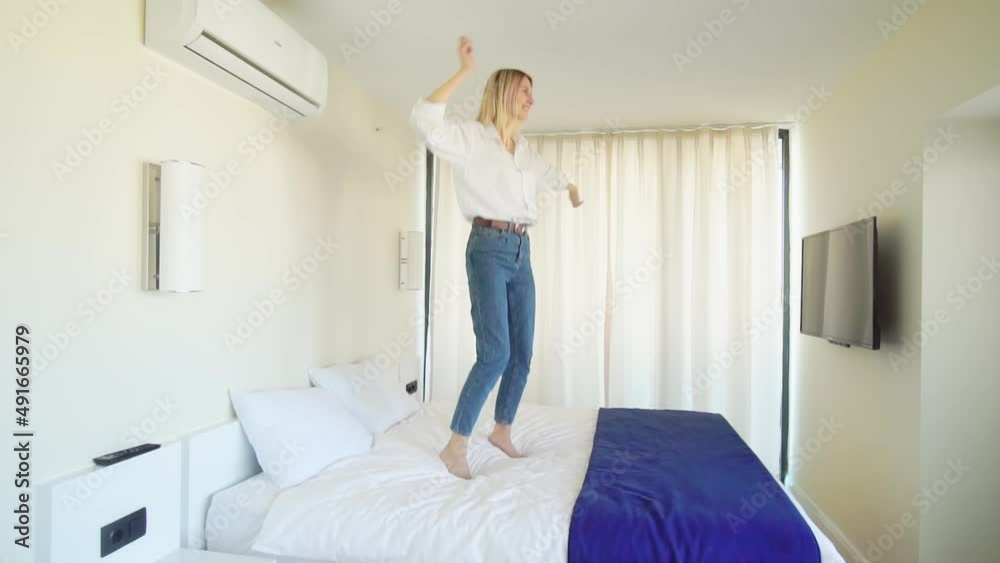 a young beautiful slender Caucasian woman dances to her favorite disco music, jumps on the bed, enjoying a free weekend vacation alone in a hotel bedroom or her apartment. Joyful and happy life. a young beautiful slender Caucasian woman dances to her favorite disco music, jumps on the bed, enjoying a free weekend vacation alone in a hotel bedroom or her apartment. Joyful and happy life.