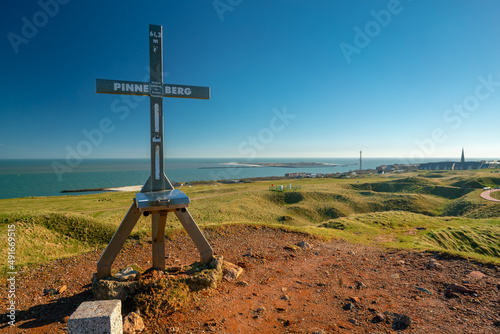 Iron cross on top of Pinneberg, the highest point of the island of Helgoland. Beautiful sunny day of winter in German archipelago with Northern sea and Dune island in the back.