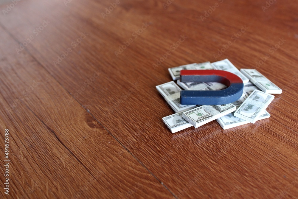 Magnet on top of pile of money. Wooden background. Copy space for text. Business and finance concept Magnet on top of pile of money. Wooden background. Copy space for text. Business and finance concept