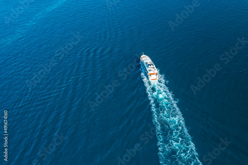 Yacht sails on Adriatic sea leaving white sea foam trace. Calm ripple on water surface illuminated by bright and warm sunlight. Aerial panorama