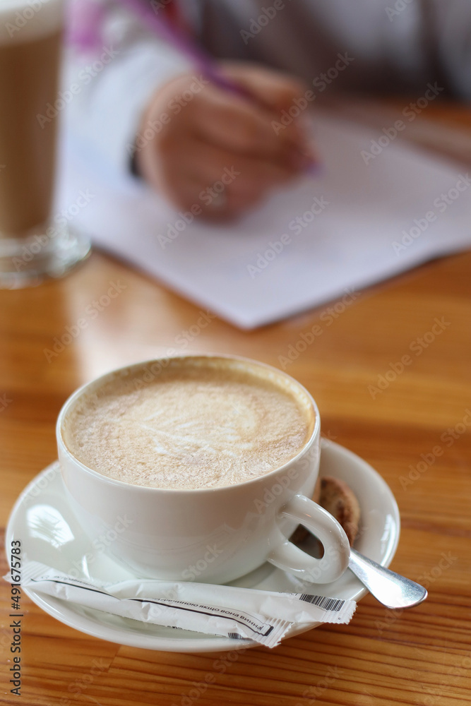 Woman in a bright skirt whiting on a paper with a cup of coffee on the table. Freelance work concept Woman in a bright skirt whiting on a paper with a cup of coffee on the table. Freelance work concept