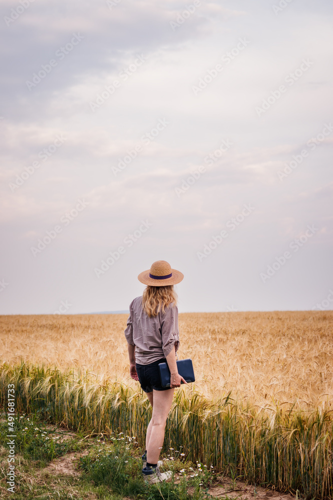 Farmer examining and looking at agricultural field before harvest. Woman with straw hat and digital tablet standing in barley field Farmer examining and looking at agricultural field before harvest. Woman with straw hat and digital tablet standing in barley field