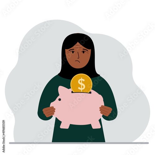 Sad muslim woman holds a piggy bank, a coin falls into the piggy bank. The concept of saving finance, savings, investing finances.