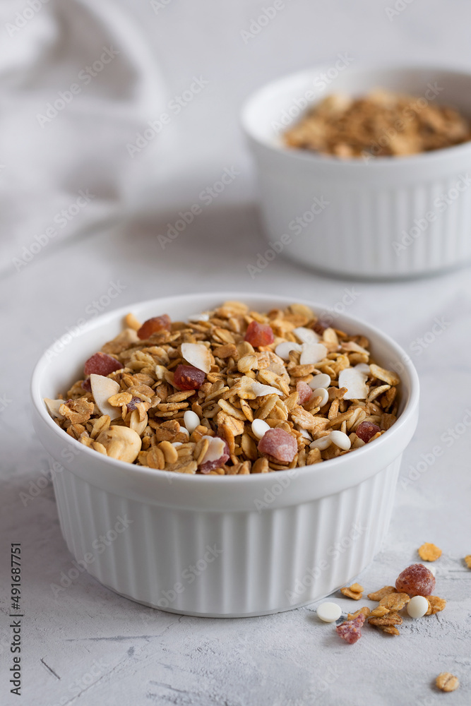 A white bowl with homemade granola on a light table. Granola with nuts and dried fruits for a healthy breakfast. Close-up. Selective focus. A white bowl with homemade granola on a light table. Granola with nuts and dried fruits for a healthy breakfast. Close-up. Selective focus.
