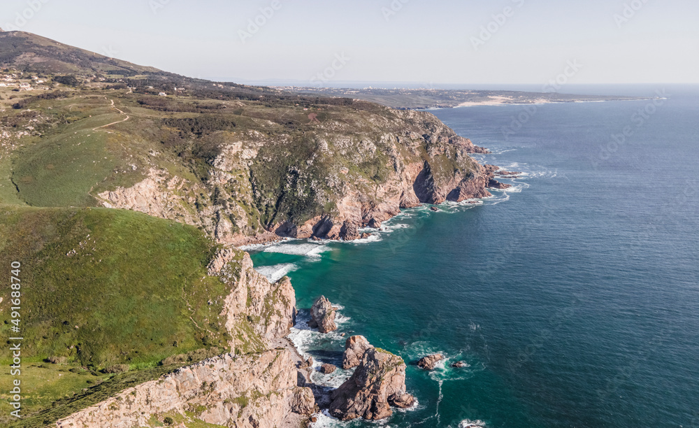 Aerial view of wild coastline with cliffs and rocky promontory near Cabo da Roca facing the Atlantic Ocean, Colares, Lisbon, Portugal. Aerial view of wild coastline with cliffs and rocky promontory near Cabo da Roca facing the Atlantic Ocean, Colares, Lisbon, Portugal.
