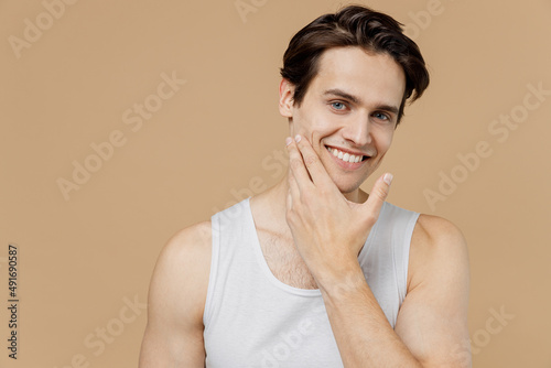 Εκτύπωση καμβά Attractive smiling calm young man 20s perfect skin wearing bundershirt touch face after shaving isolated on pastel pastel beige background studio