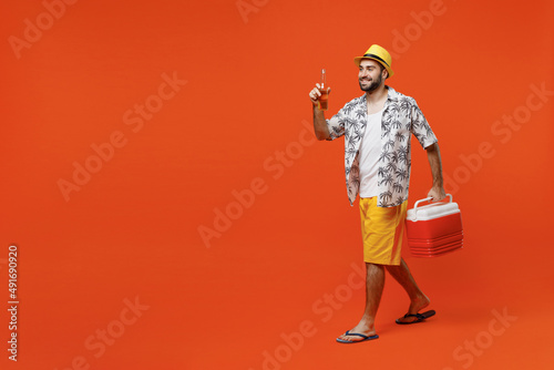 Young side view happy cool tourist man 20s in beach shirt hat hold beer bottle alcohol cooler box fridge isolated on plain orange background studio portrait. Summer vacation sea rest sun tan concept.