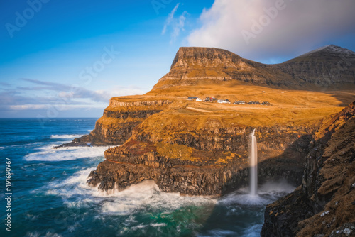 Sunny view of Mulafossur waterfall with Gasadalur village on background. Vagar island, Faroe Islands, Denmark. November 2021. Lonf exposure picture © Сергій Вовк