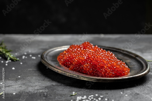 Red caviar in metal plate on dark background. Gourmet food close up, appetizer, selective focus, banner, menu, recipe place for text