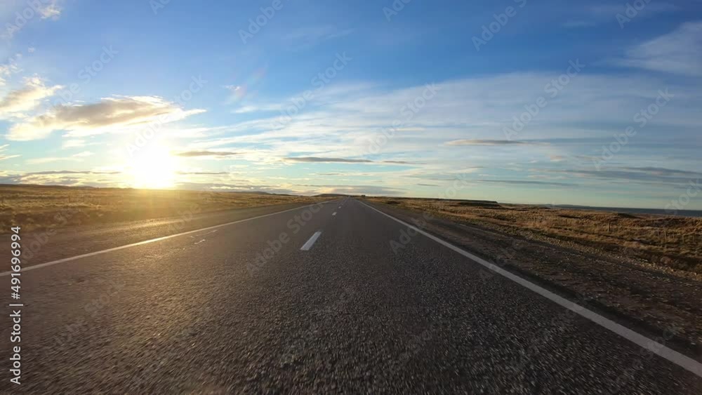 Point of view of a car driving along the asphalt road in the yellow field at sunset.