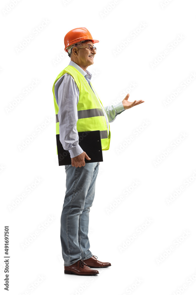 Full length profile shot of a male engineer with a safety vest and hardhat gesturing with hand