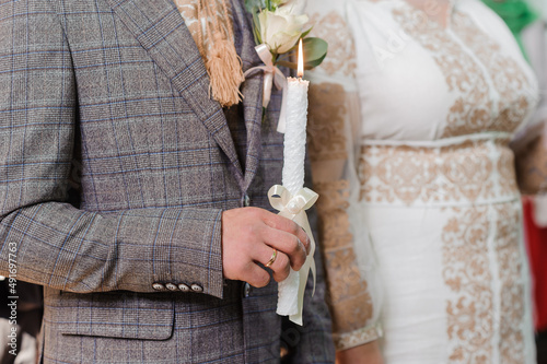 The bride and groom hold shining candles during the ceremony in the church. Hands of newlyweds with candles in the church. Church religious details. Traditions © Galka3250