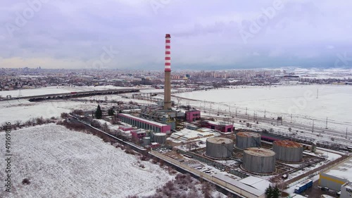 The thermal power plant near Sofia works at full capacity in the cold snowy winter. Aerial drone shot. Smoking pipe and heat pipes.