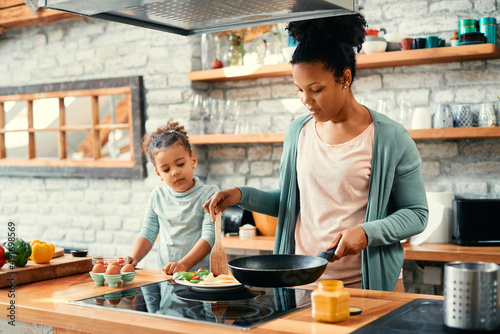 African American mother making breakfast for her daughter in the kitchen.