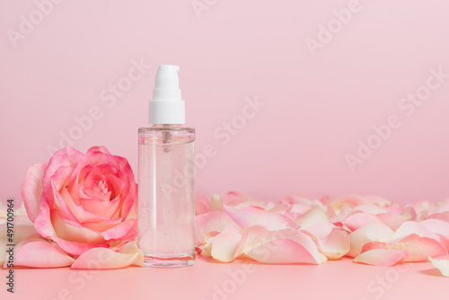 Serum bottle or facial and body gel with rose on pink background, copy space, natural skin care cosmetics