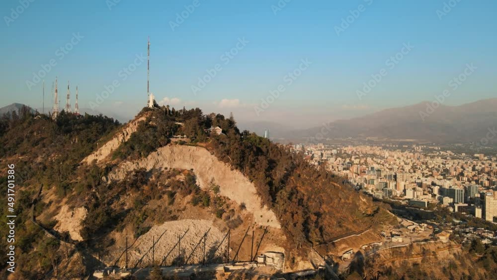 Aerial truck right of Sanctuary of the Immaculate Conception in San Cristóbal Hill and Santiago buildings un background at golden hour, Chile