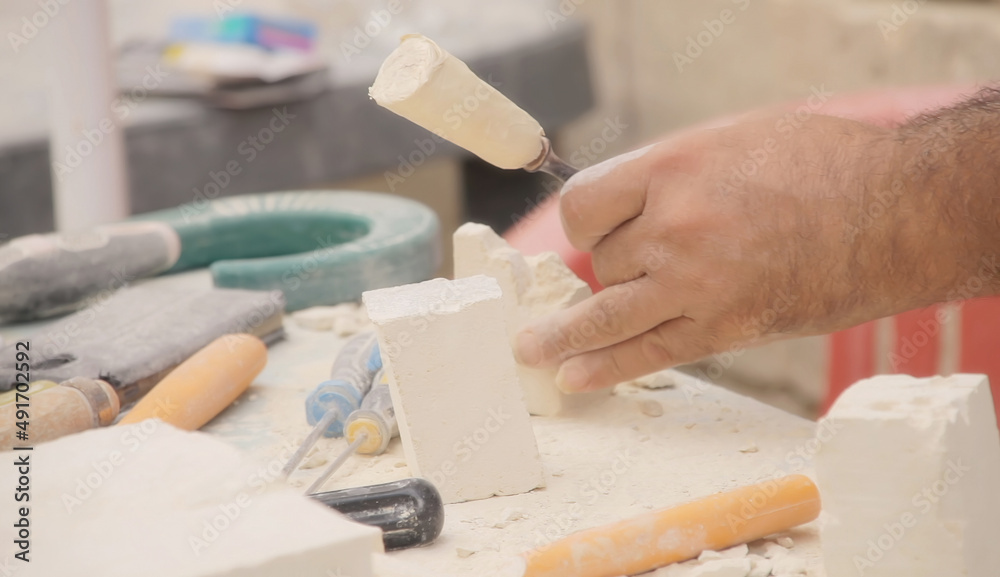 A man carving a piece of calcarenite stone (a type of of soft limestone) with a chisel, in the shape of a souvenir. Exterior day, detail closeup shot.
A man carving a piece of calcarenite stone (a type of of soft limestone) with a chisel, in the shape of a souvenir. Exterior day, detail closeup shot.
