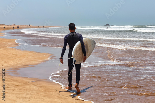 Canvas Print Unknown man in a wetsuit walking holding a surfboard in his hands along the Atlantic coast