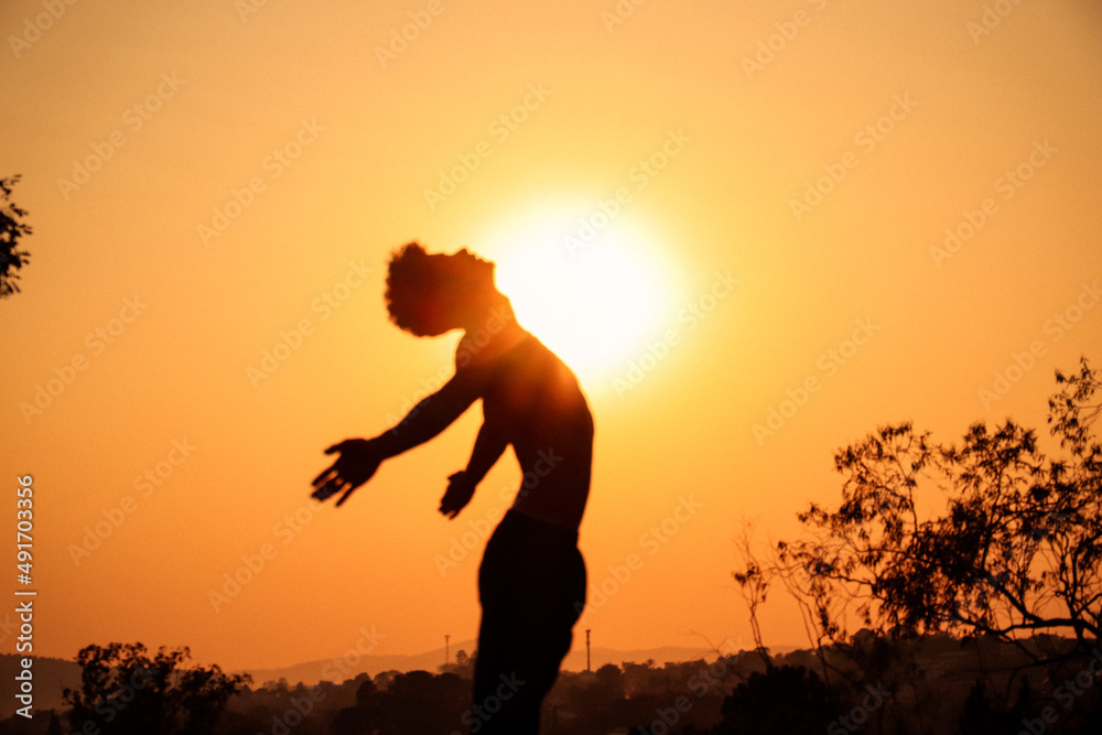 Young man silhouette doing yoga at the sunset on a top of the mountain with the sun behind with arm wide open