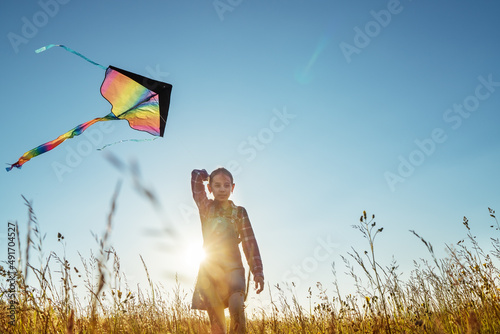 9YO Smiling girl with flying colorful kite running on the high grass meadow in the mountain fields and smiling at the camera. Happy childhood moments or outdoor time spending concept image. photo