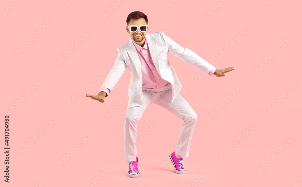 Happy millennial guy in suit and pink converse dance on pink studio background. Smiling stylish young Caucasian man in formalwear and tennis shoes make moves have fun. Fashion and style. Stock Photo