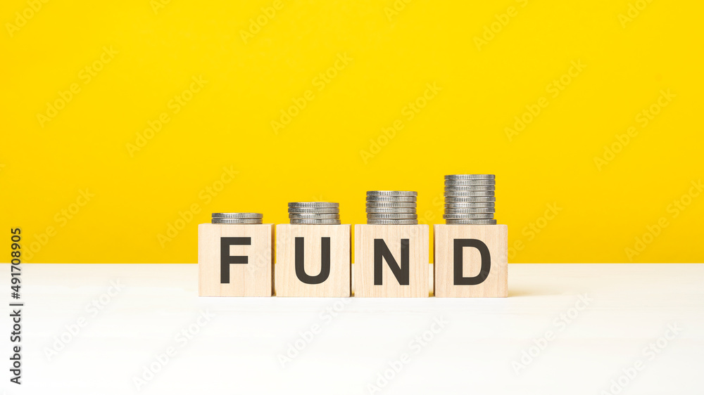 wooden cube on a concrete surface with text Fund. copy space on right for design, yellow background wooden cube on a concrete surface with text Fund. copy space on right for design, yellow background