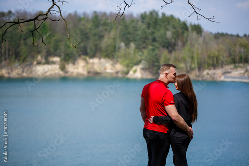 Happy and young girl and guy holding hands and laughing  on the background of a lake and a green meadow. A couple is standing in a meadow. Joyful summer day