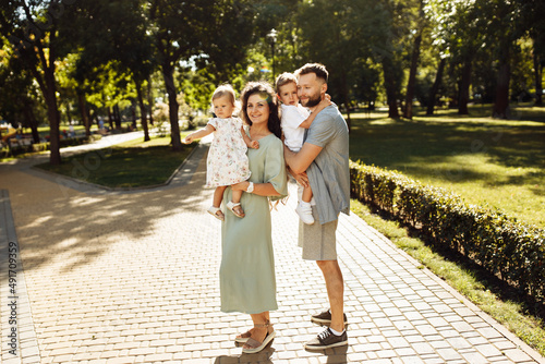 Happy parents with little kids at the park, caring dad hold in arms adorable daughter, beautiful mom hold joyful son, loving husband gentle kiss lovely wife, family concept © shunevich