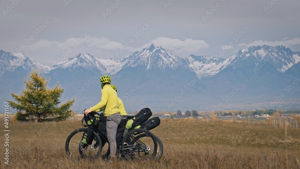 The man and woman travel on mixed terrain cycle touring with bikepacking. The two people journey with bicycle bags. Sport bikepacking, bike, sportswear in green black colors. Mountain snow capped. The man and woman travel on mixed terrain cycle touring with bikepacking. The two people journey with bicycle bags. Sport bikepacking, bike, sportswear in green black colors. Mountain snow capped.