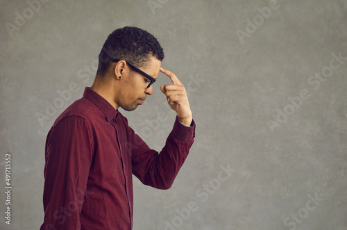 Fototapeta Naklejka Na Ścianę i Meble -  Young african american man thinking put finger to forehead studio portrait headshot. Black businessman freelancer brainstorming searching problem solution and inspiration. Side view