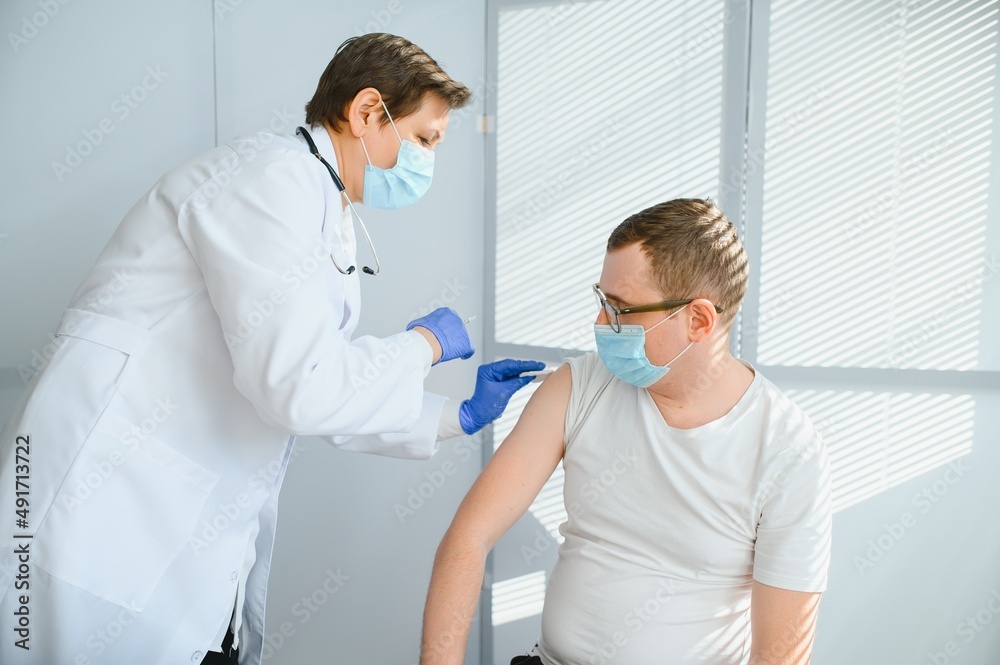 Obraz premium Female doctor making injecting using syringe to male patient in hospital. Senior man taking injection for flu in clinic. Female doctor vaccinating a man.