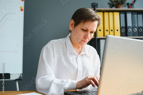 Smiling stylish mature middle aged woman sits at desk with laptop, portrait. older senior businesswoman..