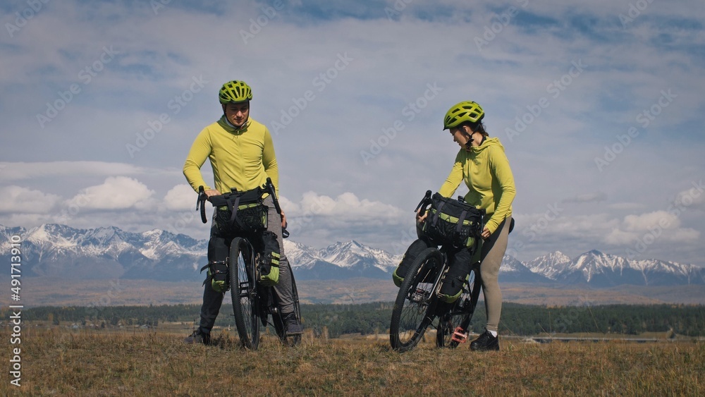The man and woman travel on mixed terrain cycle touring with bikepacking. The love couple journey with tent in nature with bicycle bags. Stylish bikepacking, bike, sportswear in green black colors. The man and woman travel on mixed terrain cycle touring with bikepacking. The love couple journey with tent in nature with bicycle bags. Stylish bikepacking, bike, sportswear in green black colors.