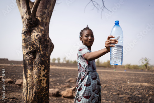 Cute African village girl with a big mouthful of water in her mouth and holding aloft a plastic bottle  recommending the use of clean and fresh drinking water  disease prevention concept