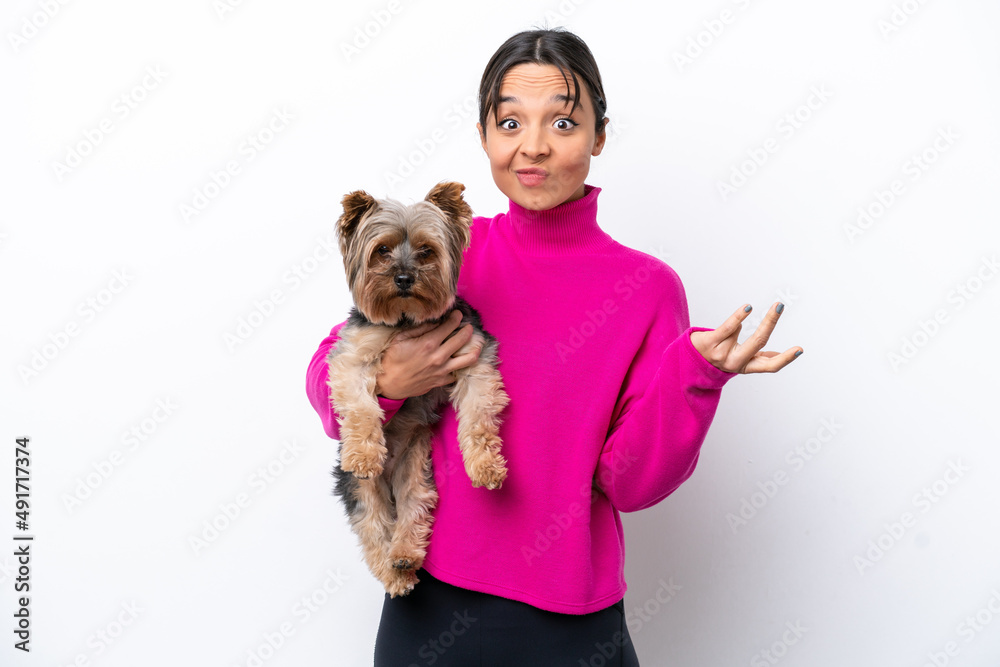 Young hispanic woman holding a dog isolated on white background making doubts gesture while lifting the shoulders Young hispanic woman holding a dog isolated on white background making doubts gesture while lifting the shoulders