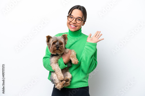Young hispanic woman holding a dog isolated on white background saluting with hand with happy expression