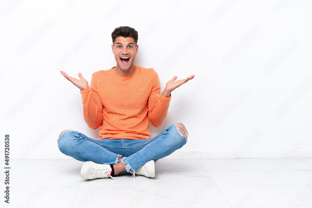 Young man sitting on the floor isolated on white background with shocked facial expression