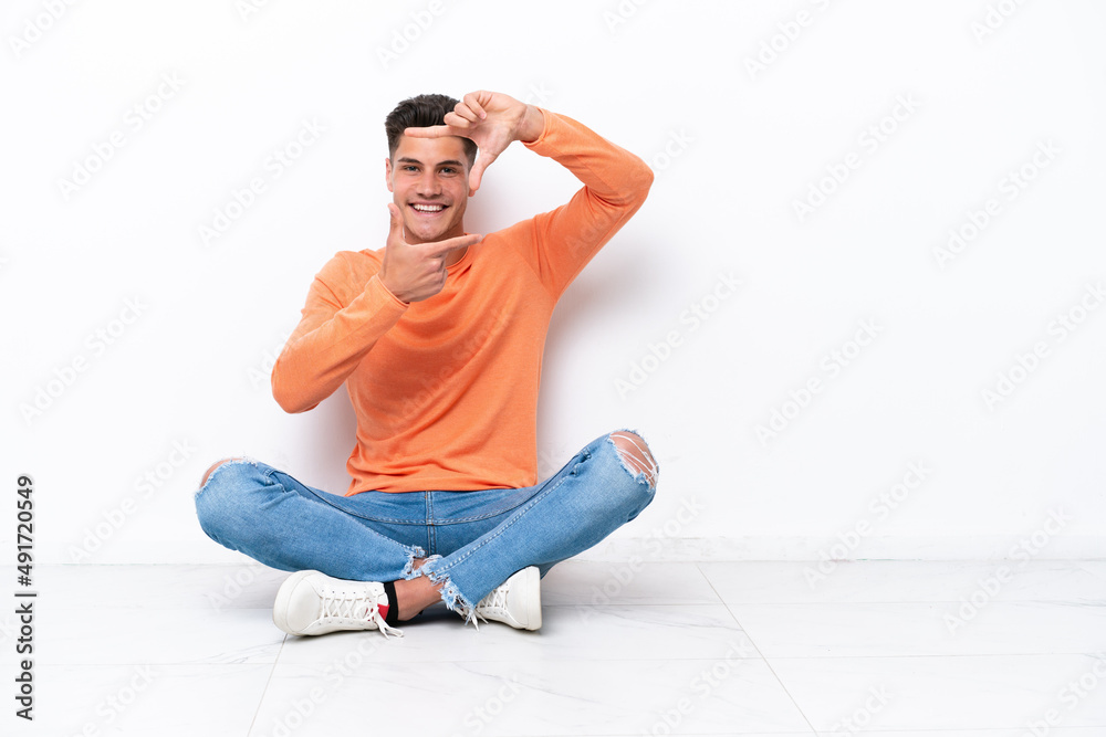 Young man sitting on the floor isolated on white background focusing face. Framing symbol